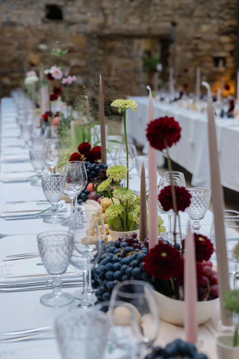 Wedding breakfast table with burgundy flowers, fruit and taper candles