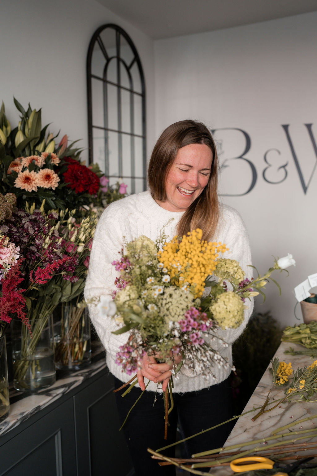 Bramble & Willow florist holding a seasonal flower arrangement in the studio