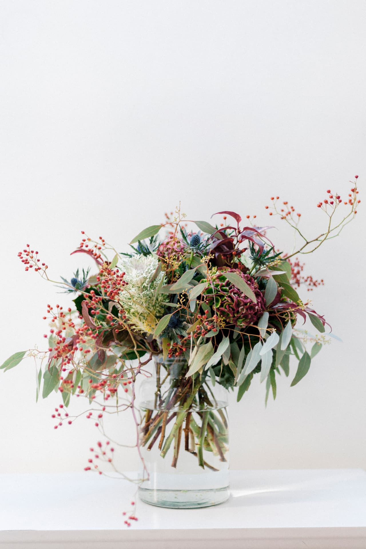Seasonal bouquet with rosehips, eucalyptus and deep burgundy flowers in a glass vase