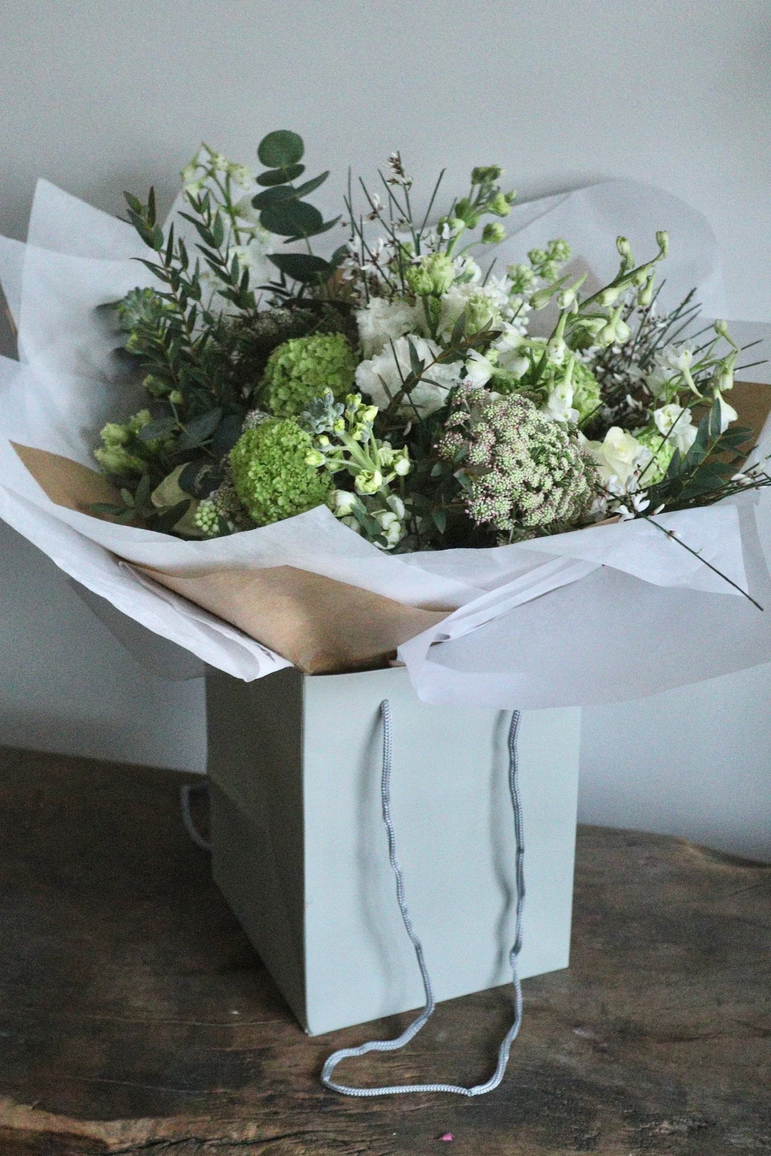 White seasonal flowers with natural foliage in a hand-tied bouquet