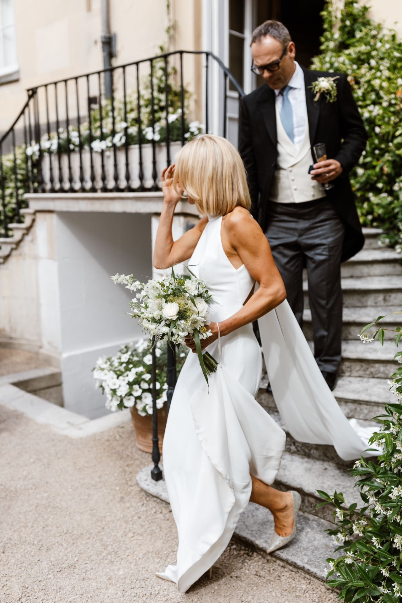 Bride carrying a white and green bouquet while descending a flower-lined staircase