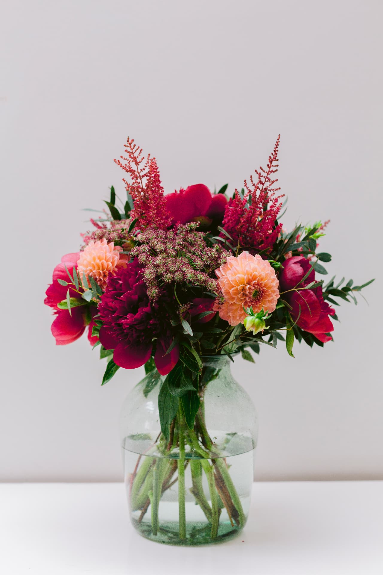 Seasonal arrangement of deep pink flowers and peach dahlias in a glass vase
