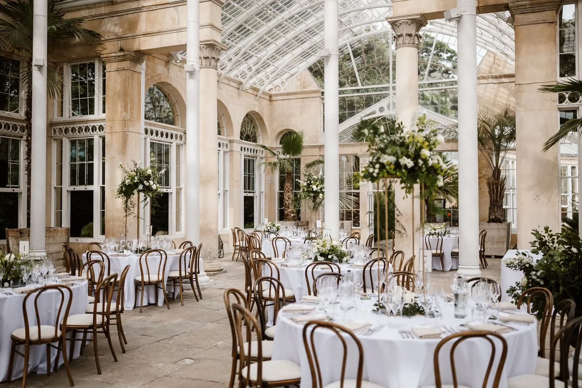 Glasshouse wedding reception with tall white and green arrangements