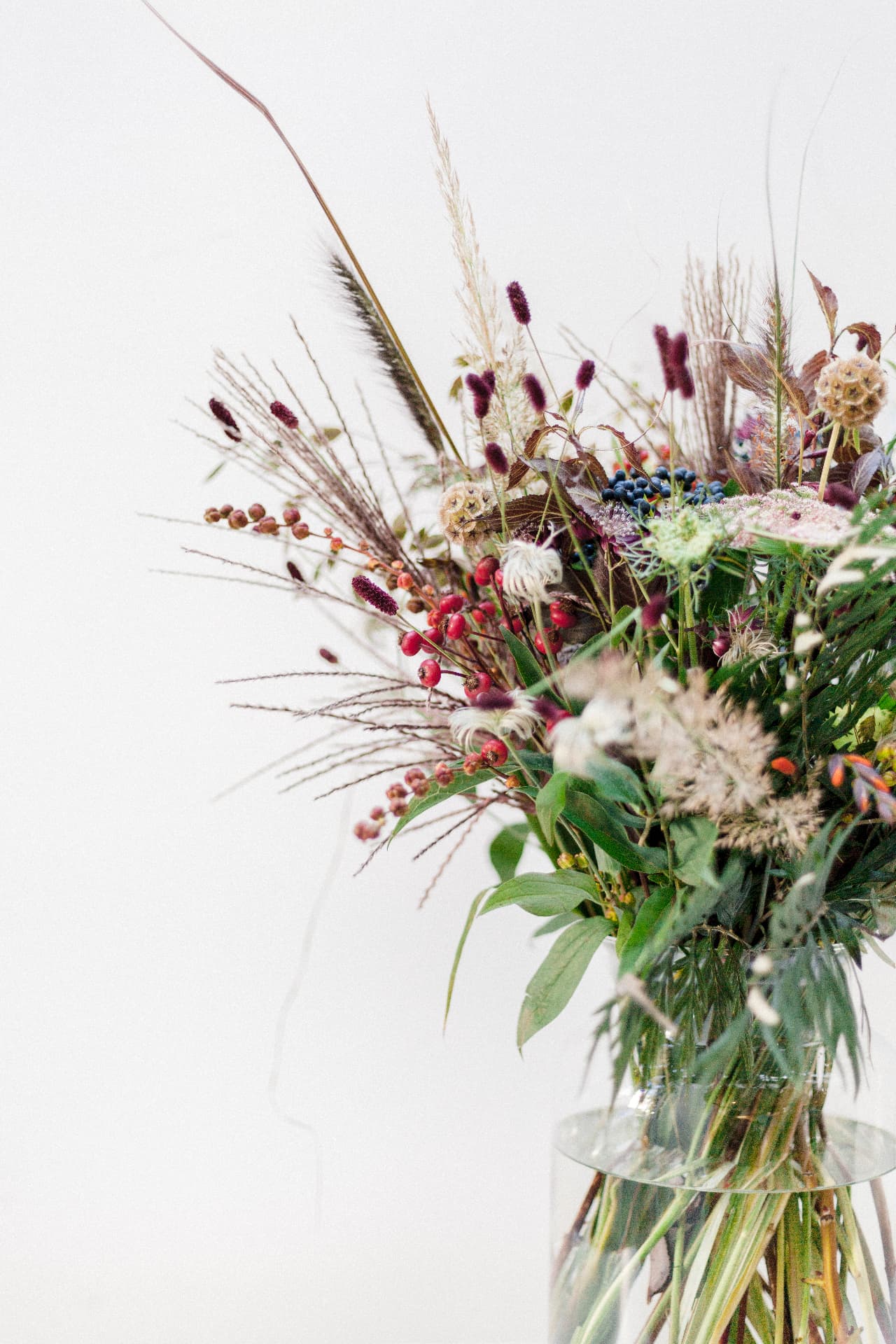 Textural autumn flower arrangement with rosehips, grasses and deep burgundy flowers