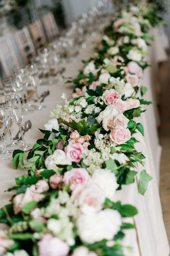 Long wedding table edged with pink roses and greenery