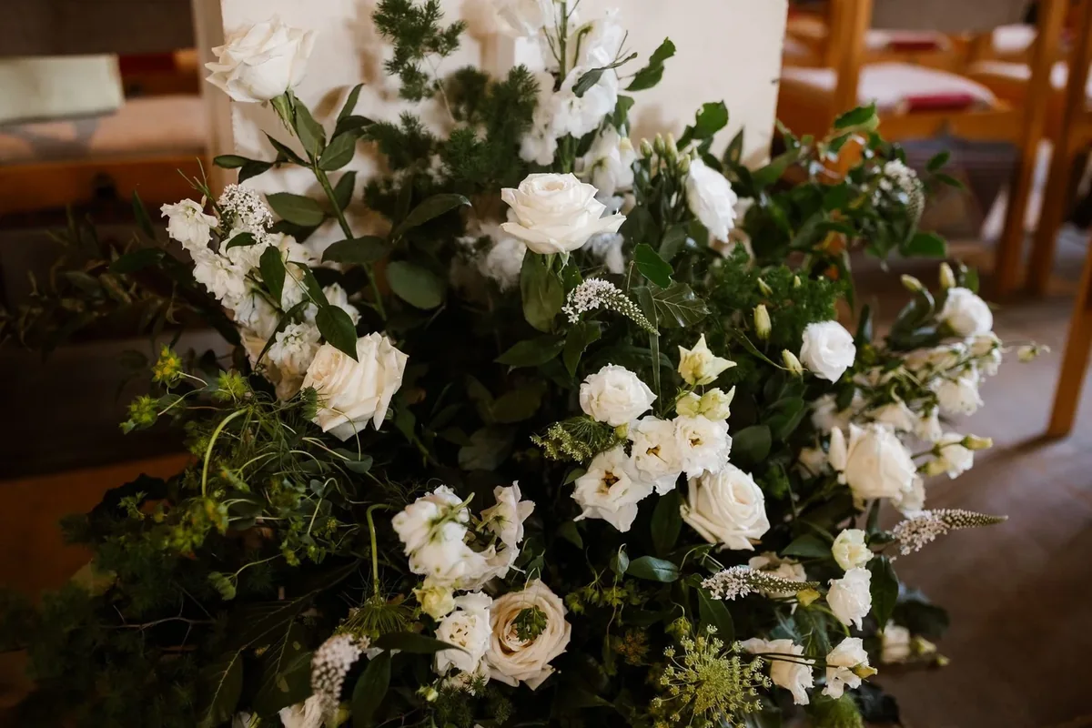 White and green ceremony flowers arranged beside church seating