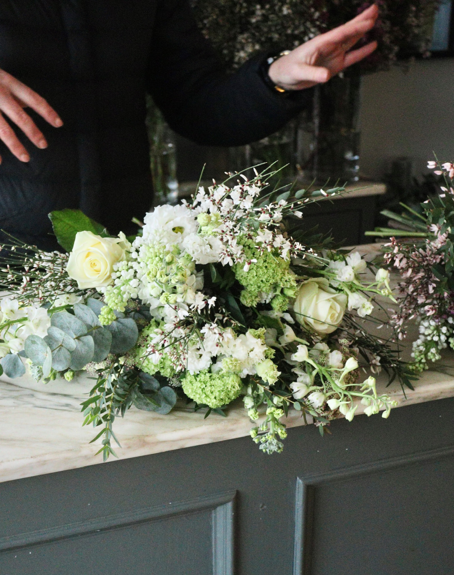 White and green seasonal flowers being arranged by Bramble & Willow