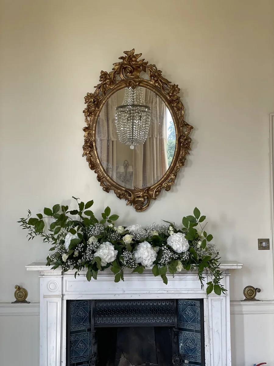 White and green mantel arrangement beneath a gilt mirror